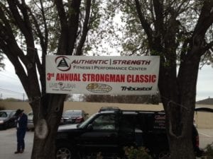 White banner for strongman competition hung between two trees
