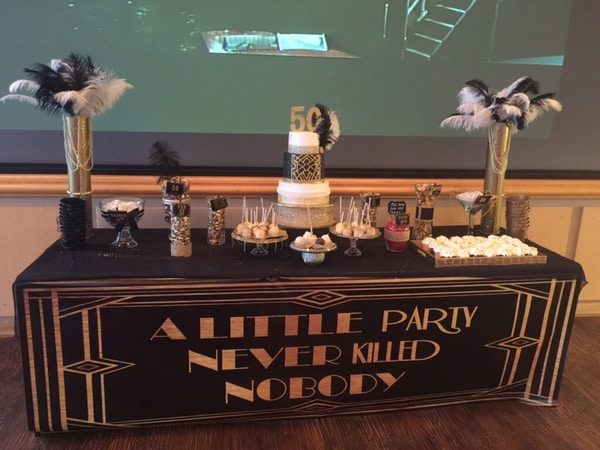 Black banner with silver lettering hanging from a table with decorations and a birthday cake