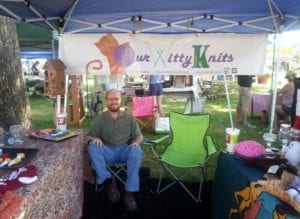 Man in chair under tent at a booth for a knitting company